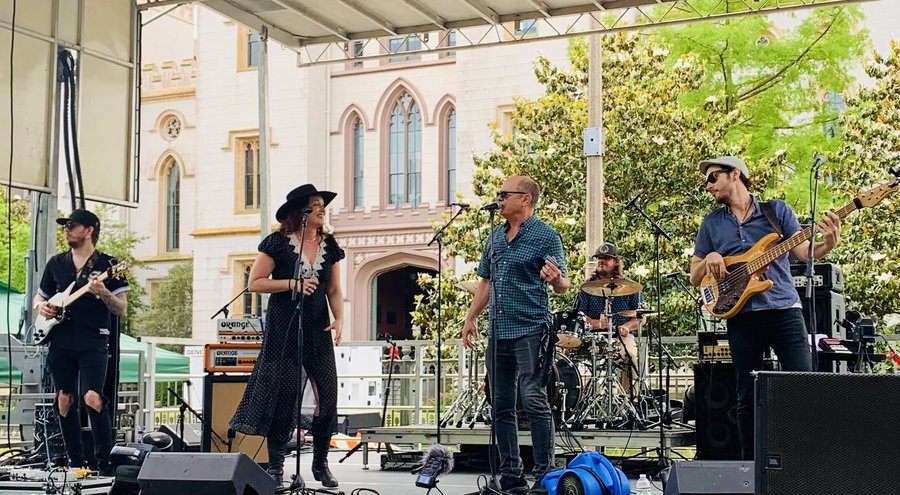 Sariah Storm and The Mysteries performing on an outdoor stage, five musicians with guitar, bass, drums and harmonica