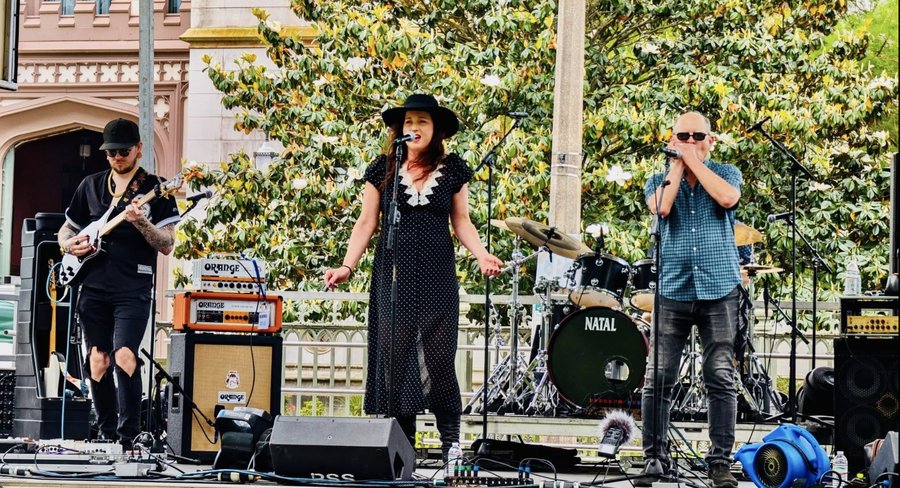 Three members of the band on stage, guitarist, Sariah singing at the microphone, and harmonica player