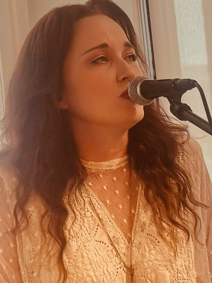 Sariah Sizemore singing into a microphone in warm light, wearing a cream lace blouse